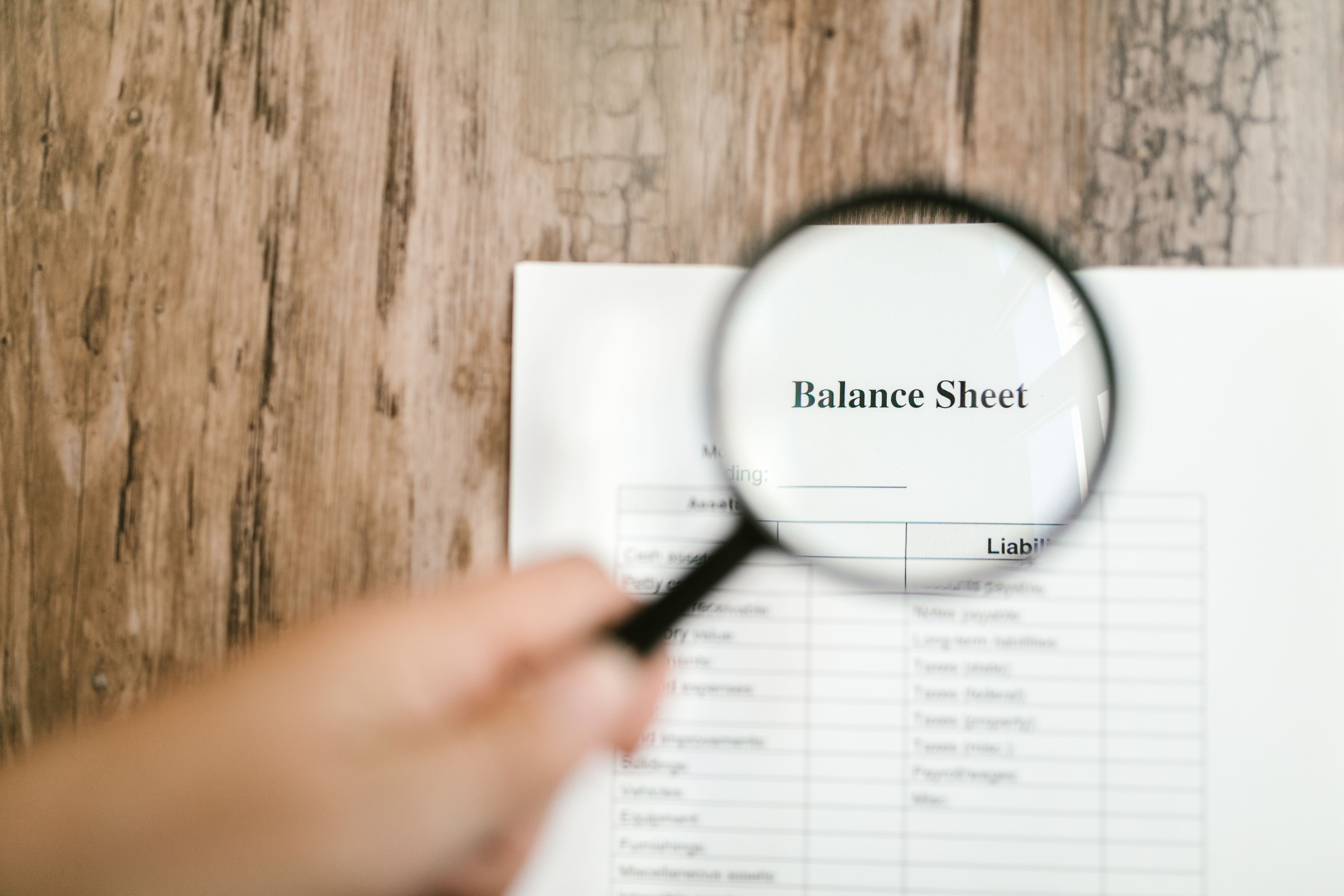 Balance sheet document under a magnifying glass representing scrutiny of official assets