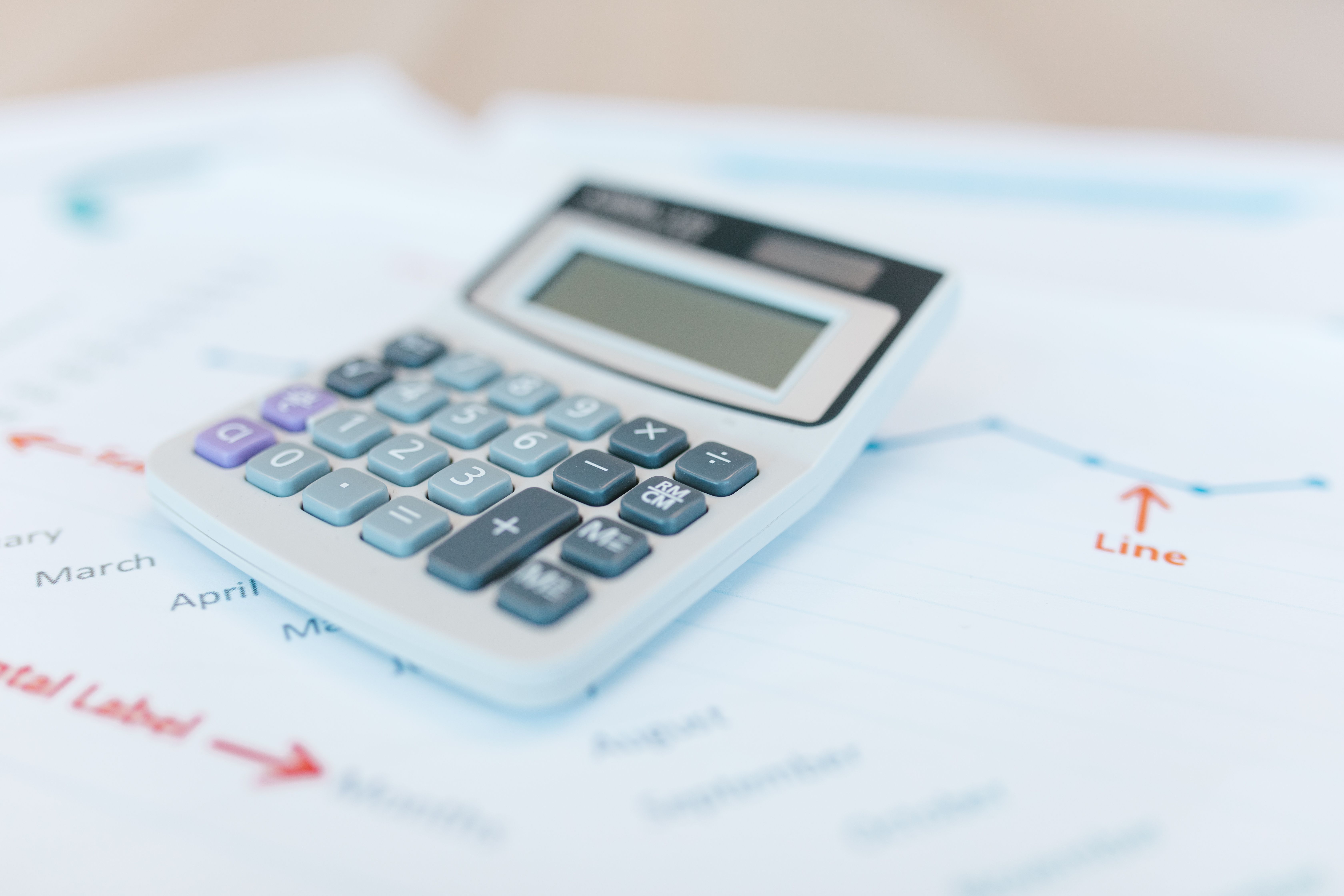 Calculator resting on financial documents and graphs for budgeting and performance analysis.